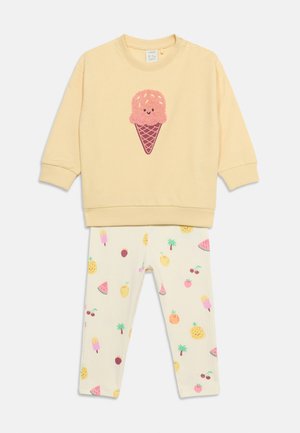 Cremefarvet langærmet top med pink isvaffel-grafik, kombineret med hvide leggings med flerfarvede frugt- og ispindsmønstre.