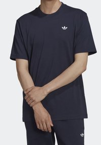 Marinblå t-shirt i bomull med korta ärmar och rundad hals. Har en vit Adidas-logga på bröstet. Slät textur, avslappnad passform.