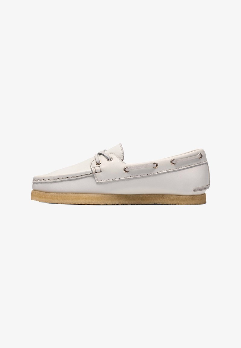 Mocassin en cuir blanc avec laçage latéral, motif cousu sur la pointe, et semelle crêpe marron clair, présenté en profil sur fond blanc.