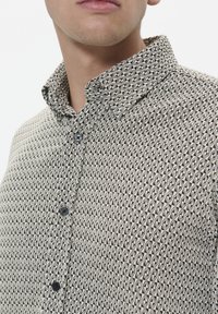 Cămașă cu mânecă scurtă, cu butoane, prezentând un model geometric în nuanțe de negru și bej, cu guler deschis și nasturi închis.