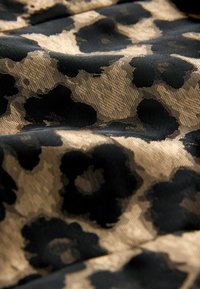 Melnas un zelta rakstu audums ar teksturētu, ziedu dizainu, kam ir mīkstas, plūstošas krokas, izceļot kontrastējošas krāsas un smalkas detaļas.