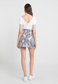 Top blanco de canalé con un pronunciado escote en la espalda, combinado con una falda mini ajustada que presenta un diseño de estampado de serpiente en gris y blanco, y un cierre en la parte posterior.