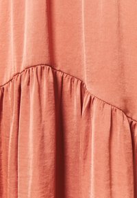 Mjukt, korallfärgat tyg med en slät textur, som har rynkad detalj och en lätt glans, vilket skapar en flödande drapering.