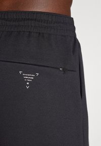 Shorts de sport noirs en tissu doux avec une taille élastique. Comprend une poche zippée et un logo imprimé sur le côté.