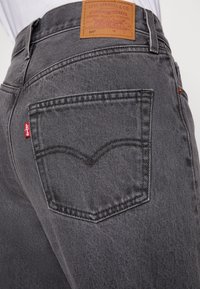 Gros plan de la poche arrière grise d'un jean Levi's avec une étiquette en cuir Levi's et une étiquette en tissu rouge sur le bord de la poche.