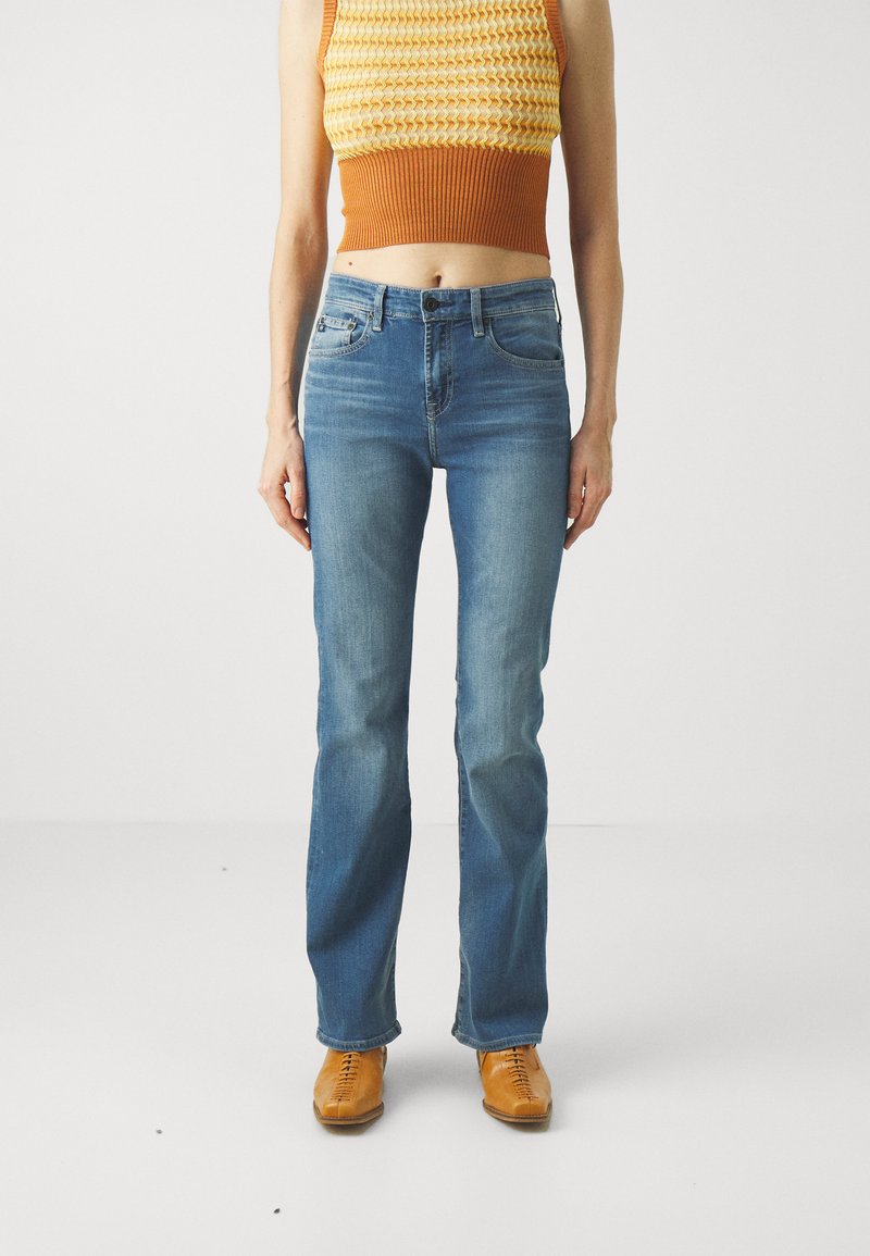 Jeans din denim decolorat, cu croială dreaptă, design cu cinci buzunare și detalii subtile de ușoară uzură, asortate cu pantofi marron cu șireturi.
