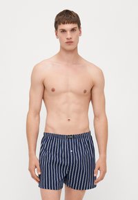 Șorturi de baie bărbați de culoare bleumarin, cu dungi verticale albe, talie elastică și detaliu cu nasture în față. Materialul pare neted și ușor.