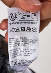 Verzorgingslabel voor kleding met de stofsamenstelling: 94% polyester, 6% spandex, wasinstructies en informatie over recycling in meerdere talen.