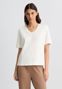 T-shirt crème en V fabriqué en mélange de coton, avec des manches courtes et des détails de logo brodés autour de l'encolure. Texture lisse.