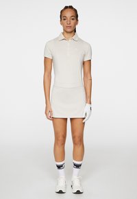 Poloklänning i ljusbeige med korta ärmar, krage och åtsittande midja. Matchas med en golfhandske och vita sneakers, accentuerad av svarta strumpor.