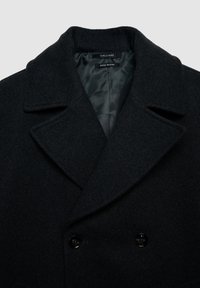 Manteau en mélange de laine croisé en gris foncé, avec un col cranté et deux boutons noirs, et une doublure en satin lisse visible à l'intérieur.