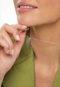 Ezüst lánc nyaklánc egyszerű kereszt medállal. A kereszt sima és polírozott, tiszta textúrával egy zöld háttér előtt.