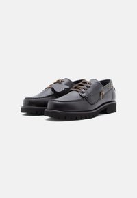 Chaussures en cuir noir avec un bout rond, des coutures décoratives, des lacets marron et une semelle en caoutchouc texturée. Détail de logo discret sur le côté.