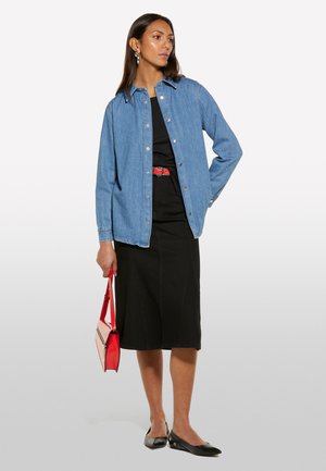 Chemise en denim, robe noire, ceinture rouge et sac à main structuré rouge. Des ballerines noires et des boucles d'oreilles en argent complètent le look. Design à coupe droite et à bouton.