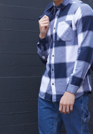 Lange mouwen geruite blouse met marineblauwe en witte ruitpatronen, knoopsluiting en een borstzak, gecombineerd met blauwe spijkerbroek.