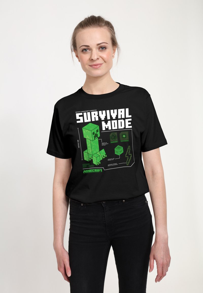 Czarny t-shirt z zielonym pikselowym wzorem postaci oraz napisem „SURVIVAL MODE” w pogrubionej białej czcionce, z elementami graficznymi związanymi z grą.