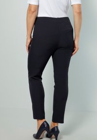 Svarta stretchbyxor med slim fit, elastisk midja och en mjuk yta. Bärs med marinblå högklackade skor. Bakvyn visas.