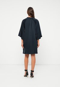 Tamsiai mėlynas kimono suknelė su alkūnių ilgio rankovėmis ir banginiu apvadu, pagaminta iš šiurkštaus audinio, krentanti virš kelių.