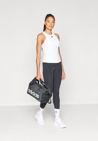 Top blanco sin mangas, leggings negros y zapatillas blancas. Bolsa de viaje negra con logo blanco "adidas". Tejido liso, diseño ajustado.