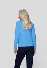 Hellblaues Sweatshirt mit langen Ärmeln und rundem Ausschnitt. Kombiniert mit dunkel gemusterten Hosen, die eine glatte Strickstruktur zeigen.