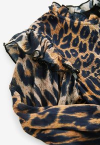 Materiał w leopardzie wzory z falbanami wzdłuż dekoltu, w odcieniach beżu, czerni i brązu; teksturowany prążkowany wzór.