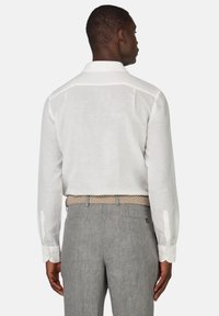 Camicia bianca a maniche lunghe con colletto classico, abbinata a pantaloni grigi chiari e una cintura intessuta beige, con polsini delle maniche abbottonati.