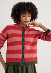 Röd och rosa randig kofta med en grön knapplist och ribbade ärmslut. Har svarta knappar och en avslappnad passform.