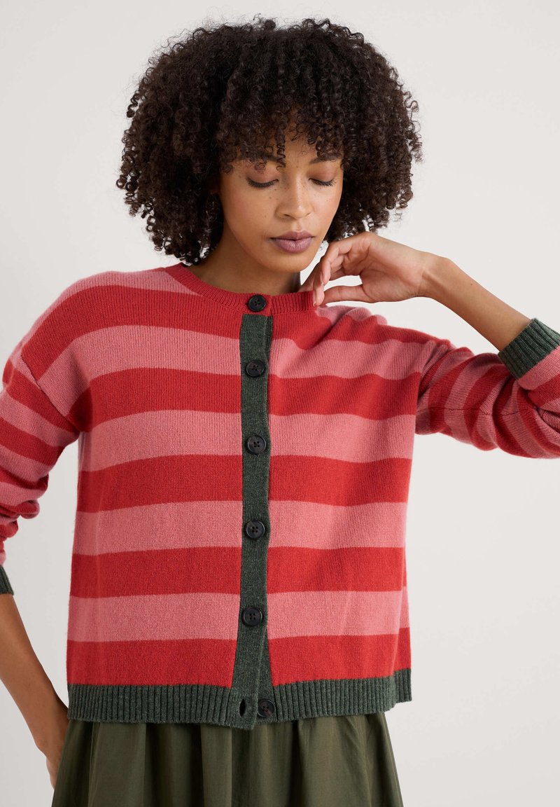 Röd och rosa randig kofta med en grön knapplist och ribbade ärmslut. Har svarta knappar och en avslappnad passform.