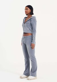 Grijze cropped hoodie met een rits, voorzien van geborduurde accenten; gecombineerd met bijpassende grijze flared joggingbroek en witte sneakers.