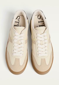 Sneakers w kolorze kremowym, wykonane z teksturowanej skóry i zamszu, z beżową gumową podeszwą i białymi sznurówkami.