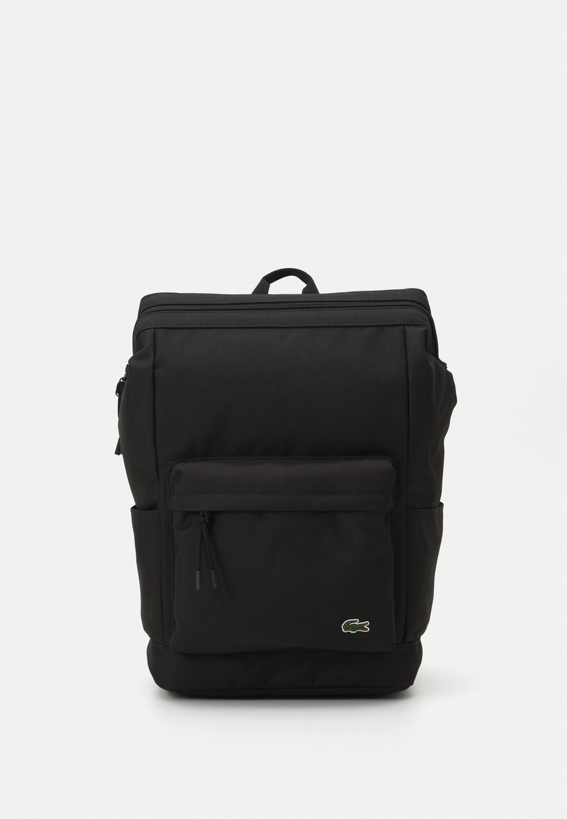 Čierny batoh, vyrobený z odolnej tkaniny, má veľkú hlavnú komoru, predné zipsové vrecko, bočné vrecká a hornú rukoväť. Viditeľné logo Lacoste.