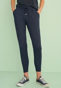 Joggers azul marino de diseño ajustado, con una cintura elástica y cordón, y bolsillos laterales. Textura de tela suave.