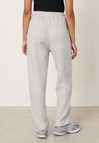 Sivé teplákové nohavice s elastickým pásom, voľným strihom a mierne ošúchaným lemom. Nosené so sivými športovými topánkami, ktoré zdôrazňujú pohodlný dizajn.