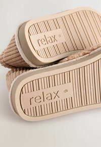 Beige Hausschuhe zum Hineinschlüpfen mit strukturierter Oberseite und gerippten Gummisohlen, auf denen das Wort "relax" eingraviert ist.