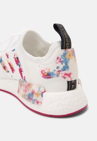White sneaker with floral patterns in pink, blue, and yellow. Textured heel accent and fabric pull tab with gold lettering. Rubber sole with pink trim.