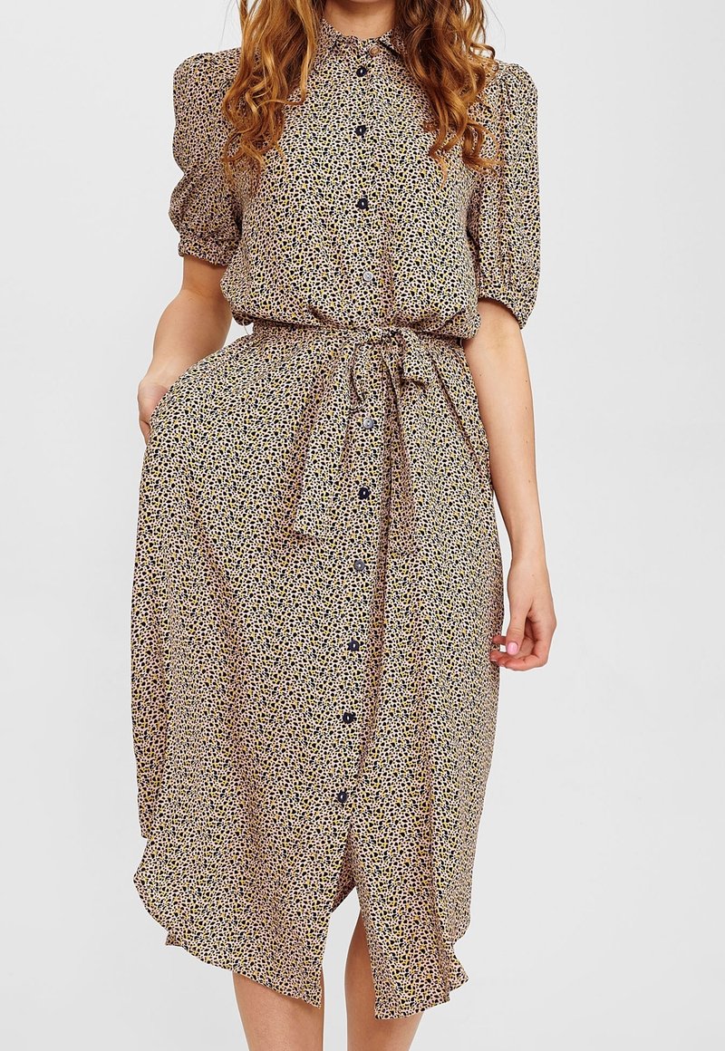 Abito midi con stampa floreale in tessuto leggero. Presenta maniche a sbuffo corte, una chiusura frontale con bottoni e una vita con lacci. I colori includono giallo, blu e crema.