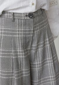 Grå ternede bukser med en struktureret stof, leggene og en sort knaplukning i taljen.