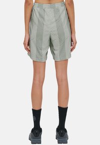 Ljusgröna shorts med en abstrakt geometrisk design, elastisk midja, mitt-lår längd, tillsammans med svarta strumpor och grå skor.