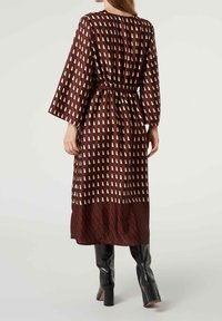 Robe midi marron à motifs avec ceinture à la taille, présentant un design géométrique en crème et brun foncé. Manches longues et texture de tissu lisse.