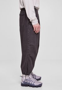 Tmavosivé, voľné nohavice s elastickým pásom a manžetami na členkoch, s bočnými vreckami. Nosené s ľahkými vzorovanými teniskami.