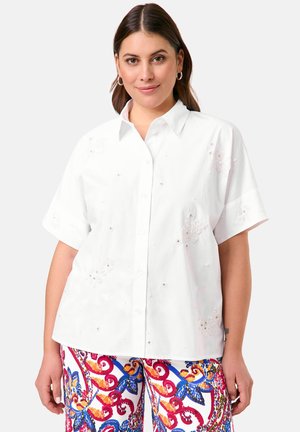 White short-sleeved shirt with a collared design, featuring floral embroidery and embellishments. Paired with colorful patterned trousers.