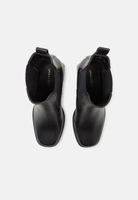 Bottes basses en cuir noir avec un bout carré et des panneaux élastiques sur les côtés. Dotées d'une languette à l'arrière pour faciliter l'enfilage. Finition texturée.