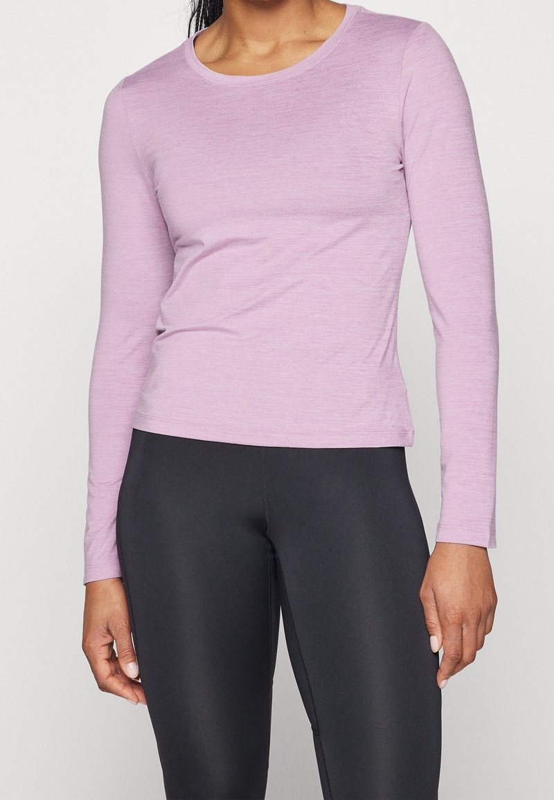 Helles lavendelfarbenes Langarmoberteil aus weichem Material, mit einem runden Ausschnitt und einer figurschmeichelnden Passform, kombiniert mit schwarzen Leggings.
