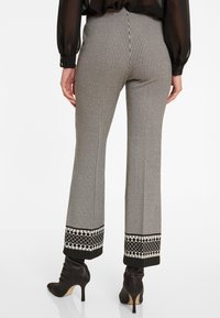 Hoch taillierte, schwarz-weiße Hahnentrittmuster-Hosen mit ausgestellten Beinen und einem dekorativen schwarzen, gemusterten Saum, kombiniert mit schwarzen Absatzstiefeln.