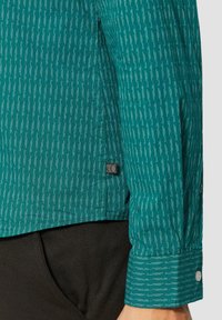 Teal button-up shirt met een verticaal gestreept patroon in het wit. Gestructureerde stof met een zichtbaar merklabel en manchet detail.