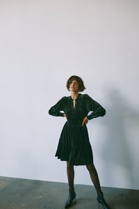 Roheline sametkleit pikade varrukatega, sügava dekolte ja kihilise äärisega. Stiilitud mustade pahkluu saapatega, neutraalse tausta ees.