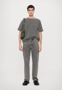 Gray oversized t-shirt and gray denim jeans, complemented by a green shoulder bag. Black shoes complete the outfit. Simple, casual design.