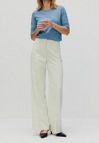 Ljusblå kortärmad tröja i kombination med högmidjade vida cremegula byxor. Svarta spetsiga skor fulländar outfiten.