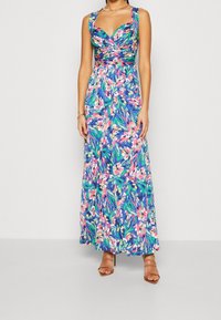 Kukkakirjailulla varustettu maxi-mekko, jossa on sininen tausta ja elävät vaaleanpunaiset ja vihreät kuviot, V-pääntie ja leveät hihnat. Kevyt kangas ja hulmuava muotoilu.