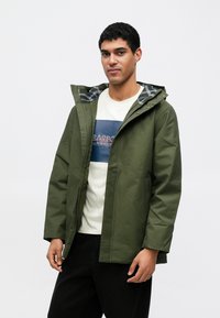 Casaco com capuz verde-oliva com fecho de correr frontal, logótipo no peito e forro às riscas. Apresenta bolsos laterais e um corte descontraído. Tecido leve.